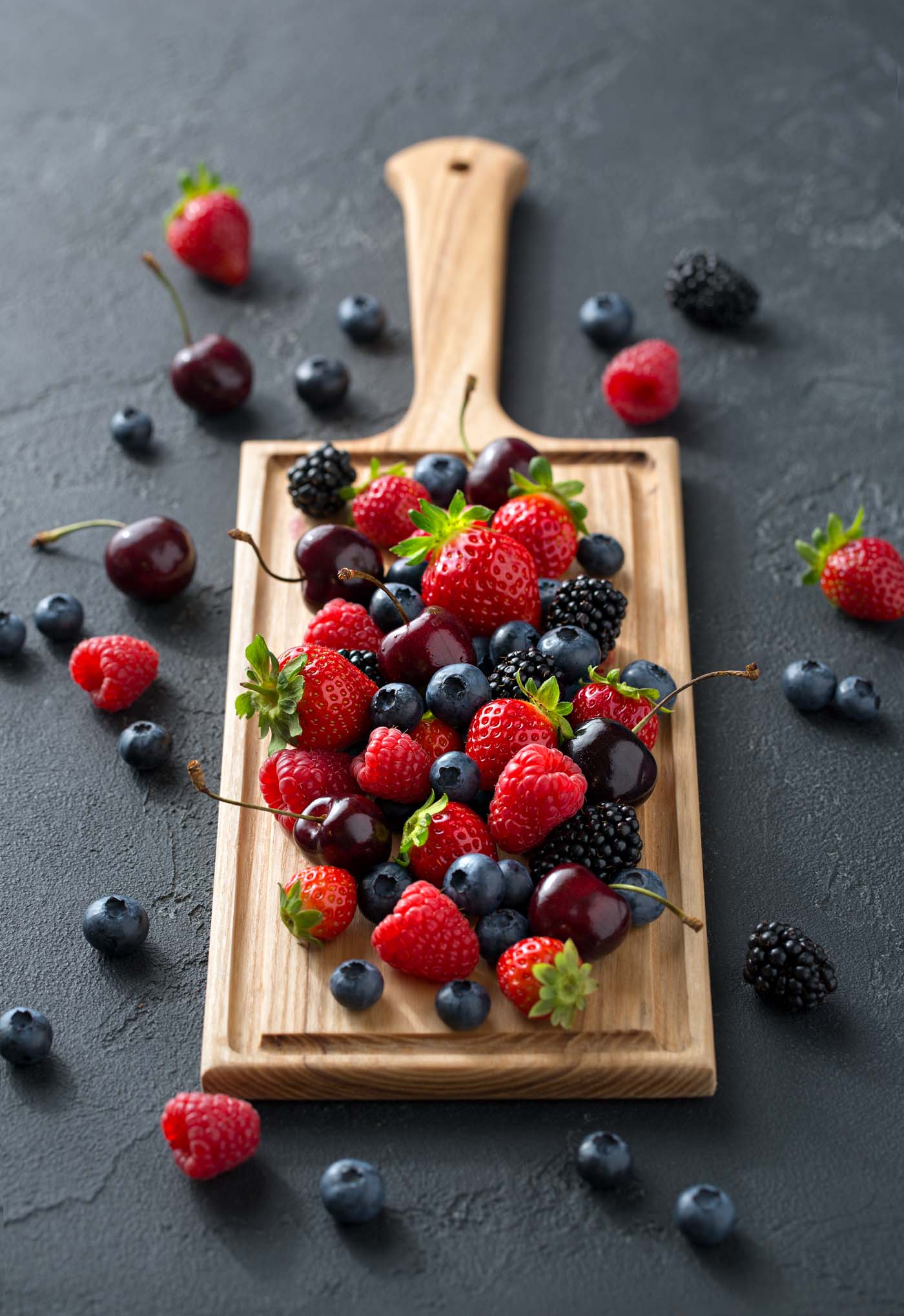 Image of a wooden chopping board covered with a variety of berries in  the centre 