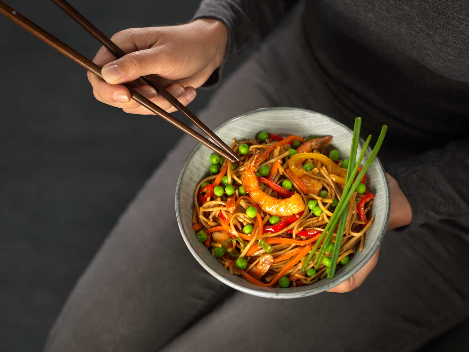 Prawn Stir Fry in a bowl with womans hands holding chopsticks 