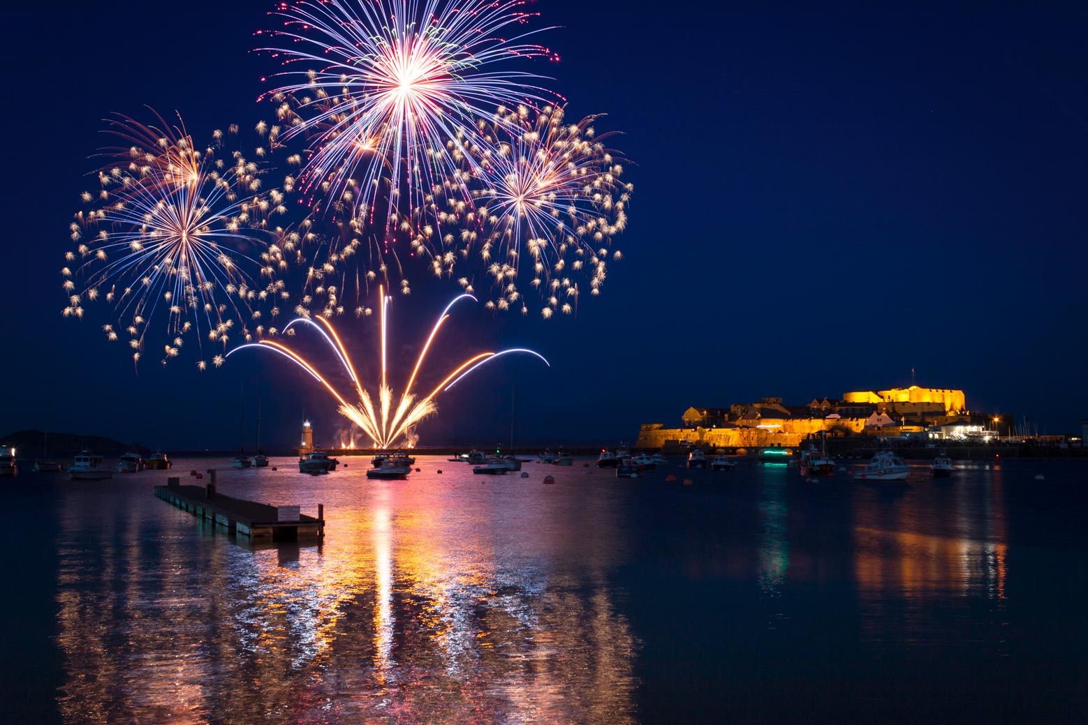 Fireworks exploding over a harbour at night